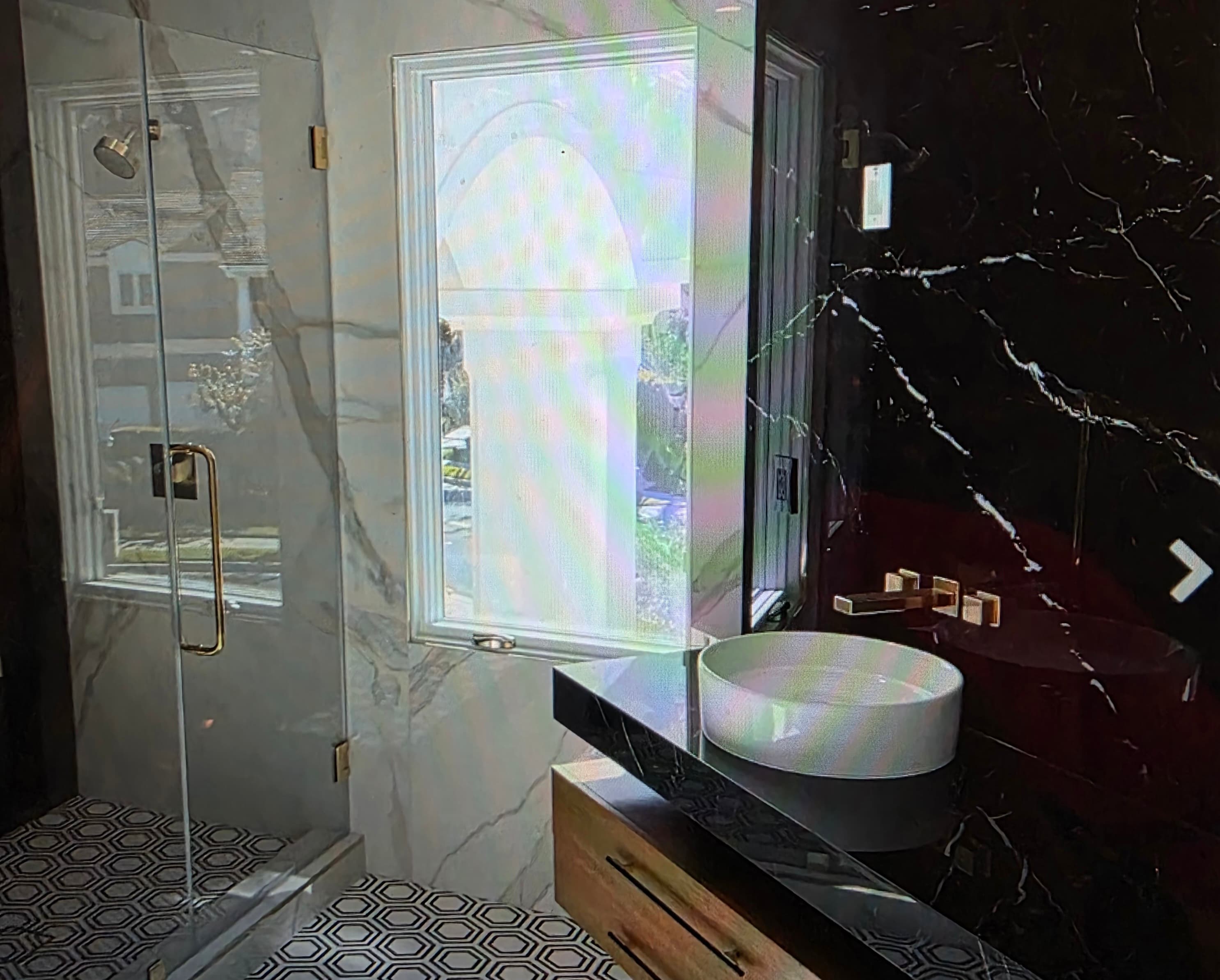 Modern bathroom with white marble walls, black marble vanity, gold fixtures, and a glass shower.
