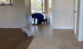 A professional worker in a blue shirt kneels to polish a shiny, light-colored tile floor.